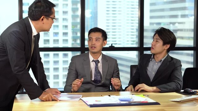 Angry boss hits the table with document paper on the table During assistant or secretary , colleague talking together. Furious business asian man smash paperwork to desk. coworker shocked, uptight.