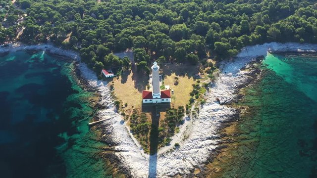 Croatia, island of Dugi Otok, panoramic view of the beautiful old lighthouse of Veli Rat on the stone shore among the pines in the morning, drone aerial circle shot