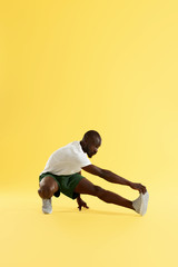Fototapeta na wymiar Man in sportswear stretching leg warming up on yellow background