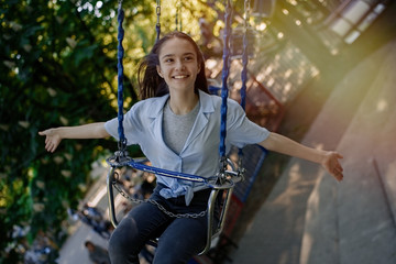 Happy child teenage girl riding chain carousel swing at amusement park    