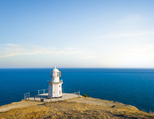 small white lighthouse on a marine cape above  evening quiet sea