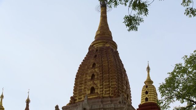 A low angle shot of golden stupas with sculptural designs at the top of a temple in Burma