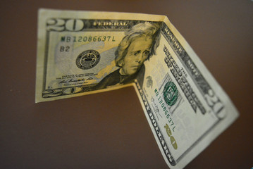 A paper note in the amount of twenty American dollars, $ 20 lies on a matte brown background....