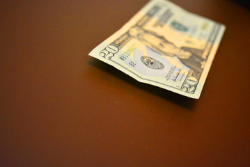 A paper note in the amount of twenty American dollars, $ 20 lies on a matte brown background....