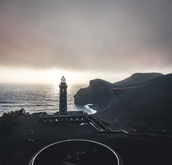 View over Capelinhos volcano, lighthouse of Ponta dos Capelinhos on western coast on Faial island, Azores, Portugal with a dramatic sunset and strong waves and clouds. Last volcano eruption was in