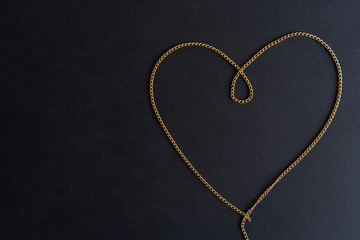 Golden chain in the shape of a heart on the black background symbolizing love. Close-up