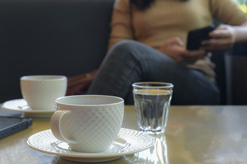 White coffee mugs patterns with background people playing mobile phone in the cafe.
