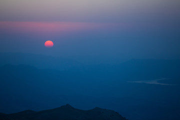 Sunrise in the mountains, deep blue sky, silhouettes of peaks and red sun disk in a light haze at Nemrut mount