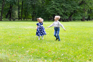 Obraz premium A boy and a girl are running around the grass, laughing and rejoicing. In the background are trees. Children are happy