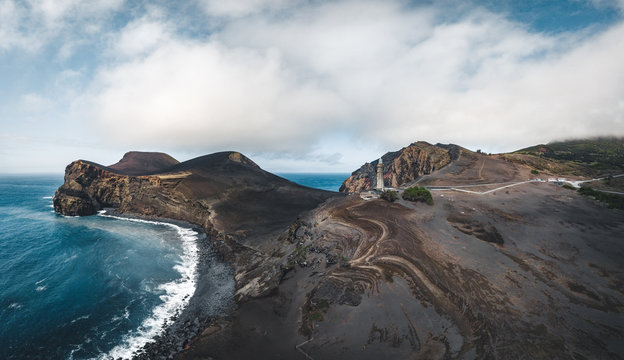 View over Capelinhos volcano, lighthouse of Ponta dos Capelinhos on western coast on Faial island, Azores, Portugal on a sunny day with blue sky and clouds and waves. Last volcano eruption was in 1957
