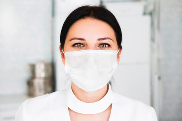 Close up portrait of young woman doctor with medical mask. Nurse looking at camera on hospital background.