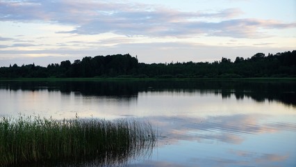 sunset over lake by forest and cloudy sky