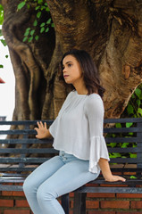 Outdoor portrait of young beautiful girl 9 to 25 years old posing in street. wearing white blouse and tight jeans and sapatillas. City lifestyle. Female fashion concept.