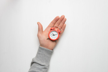 The hand of a young man holds a red alarm clock. Time, sleep, awakening concept.