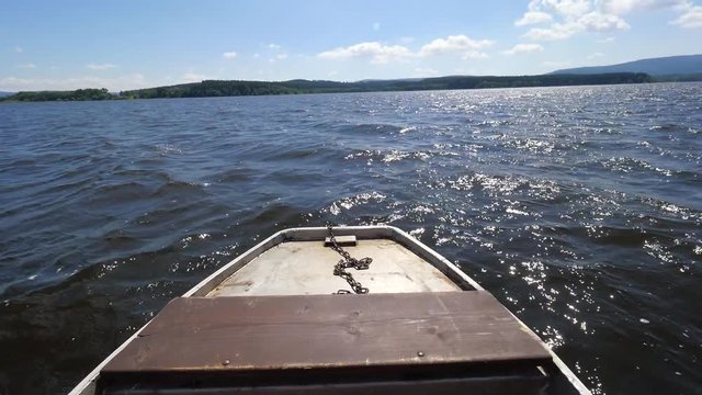 View over fishing metal boat nose against the wavy lake water and a blue sky