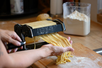 homemade noodles with small manual machine in kitchen with flour