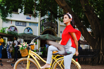 Outdoor portrait of young beautiful girl 19 to 25 years old posing in street. Brunette. riding a retro styled bicycle. Wearing red blouse With a penetrating camera look. 
