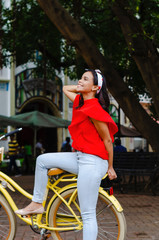 Outdoor portrait of young beautiful girl 19 to 25 years old posing in street. Brunette. riding a retro styled bicycle. Wearing red blouse With a penetrating camera look. 