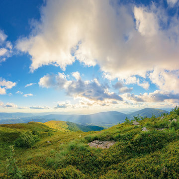 amazing summer landscape at sunset. fluffy clouds in golden light above the mountain ridge. grassy meadow on top of a hill. beautiful view in to the distance. sun on azure sky above horizon line