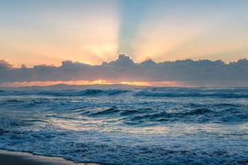 Spectacular sunrise seascape of ocean waves and sun beaming through the clouds