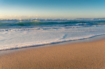 Beautiful soft waves with white foam crashing at yellow sandy shore