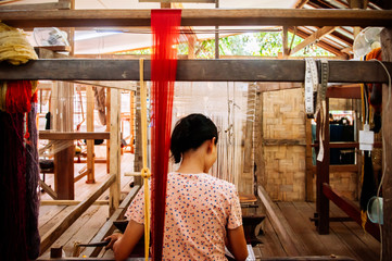Young woman working on Vintage Laos style wooden weaving loom with silk fiber