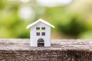 Miniature white toy model house in wooden background near green backdrop. Eco Village, abstract environmental background. Real estate mortgage property insurance dream home ecology concept