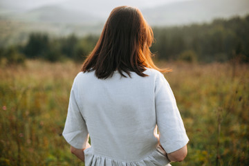 Stylish boho girl walking in grass and wildflowers in sunny meadow at  atmospheric sunset. Happy...