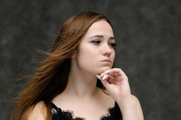 Concept close-up portrait of a pretty girl, young woman with long beautiful brown hair and beautiful face skin on a gray background. In the studio in different poses showing emotions.