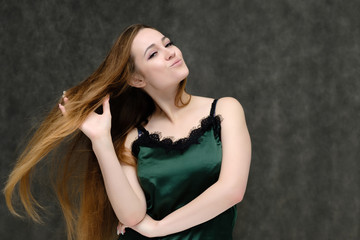 Naklejka premium Concept portrait of the waist of a pretty girl, a young woman with long beautiful brown hair and a green T-shirt on a gray background. In the studio in different poses showing emotions.