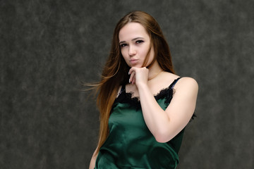 Fototapeta premium Concept portrait of the waist of a pretty girl, a young woman with long beautiful brown hair and a green T-shirt on a gray background. In the studio in different poses showing emotions.
