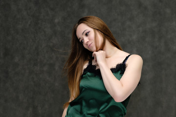 Fototapeta premium Concept portrait of the waist of a pretty girl, a young woman with long beautiful brown hair and a green T-shirt on a gray background. In the studio in different poses showing emotions.