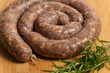Fototapeta premium Raw homemade stuffed pork sausages and rosemarin isolated on a woodboard.