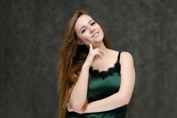 Naklejka premium Concept portrait of the waist of a pretty girl, a young woman with long beautiful brown hair and a green T-shirt on a gray background. In the studio in different poses showing emotions.