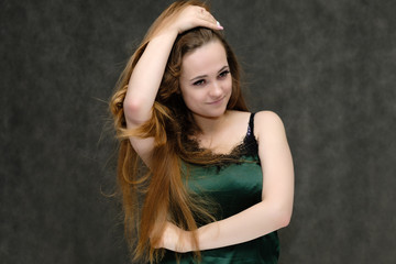 Concept portrait of the waist of a pretty girl, a young woman with long beautiful brown hair and a green T-shirt on a gray background. In the studio in different poses showing emotions.