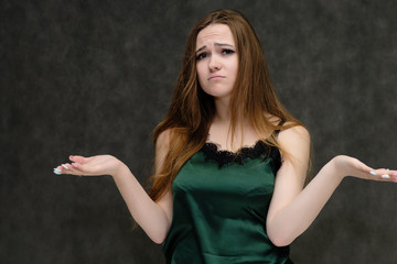 Concept portrait of the waist of a pretty girl, a young woman with long beautiful brown hair and a green T-shirt on a gray background. In the studio in different poses showing emotions.