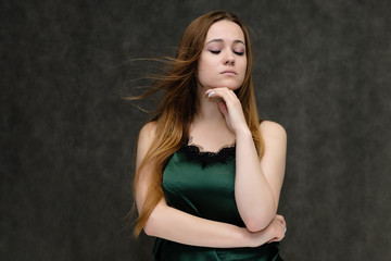 Fototapeta premium Concept portrait of the waist of a pretty girl, a young woman with long beautiful brown hair and a green T-shirt on a gray background. In the studio in different poses showing emotions.
