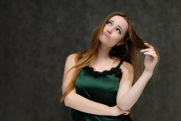 Fototapeta premium Concept portrait of the waist of a pretty girl, a young woman with long beautiful brown hair and a green T-shirt on a gray background. In the studio in different poses showing emotions.