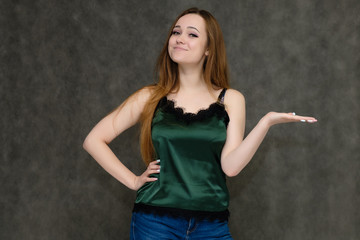 Concept portrait below belt of pretty girl, young woman with long beautiful brown hair and green t-shirt and blue jeans on gray background. In the studio in different poses showing emotions.