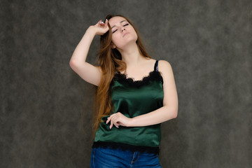 Fototapeta na wymiar Concept portrait below belt of pretty girl, young woman with long beautiful brown hair and green t-shirt and blue jeans on gray background. In the studio in different poses showing emotions.