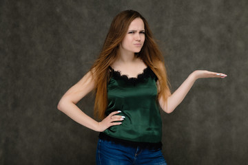 Concept portrait below belt of pretty girl, young woman with long beautiful brown hair and green t-shirt and blue jeans on gray background. In the studio in different poses showing emotions.