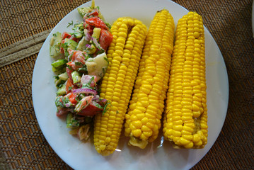 Delicious yellow sweet corn rolls with fresh vegetable salad served on a white glass plate.
