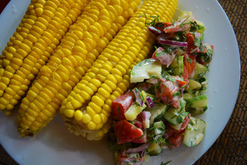 Delicious yellow sweet corn rolls with fresh vegetable salad served on a white glass plate.