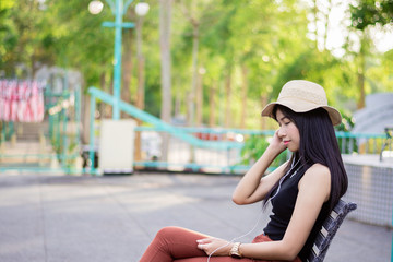 Fototapeta premium Portrait of asian women sit on the bench relaxing with green nature backgound, Girl listen musics in the morning, Rest on vacation with nature forest, Smilling and chilling girl, Lifestyle concept