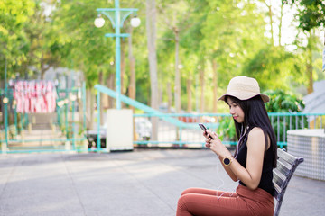 Portrait of asian women sit on the bench relaxing with green nature backgound, Girl listen musics in the morning, Rest on vacation with nature forest, Smilling and chilling girl, Lifestyle concept