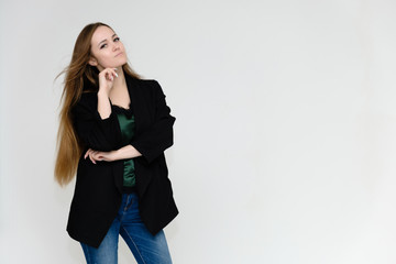 Concept portrait above the knee of a pretty girl, a young woman with long beautiful brown hair and a black jacket and blue jeans on a white background. In studio in different poses showing emotions.