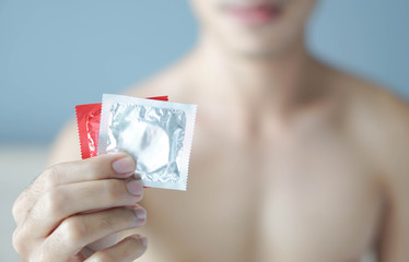 Close up man hand holding condom ready for use  lying on white bed, health care and medical concept, selective focus