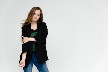 Concept portrait above the knee of a pretty girl, a young woman with long beautiful brown hair and a black jacket and blue jeans on a white background. In studio in different poses showing emotions.