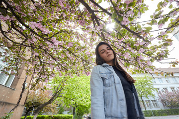 Young smiling woman posing on the background of blooming sakura