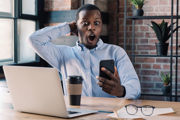 Business man using app on phone sitting in modern office, having good news on smartphone with WOW emotion